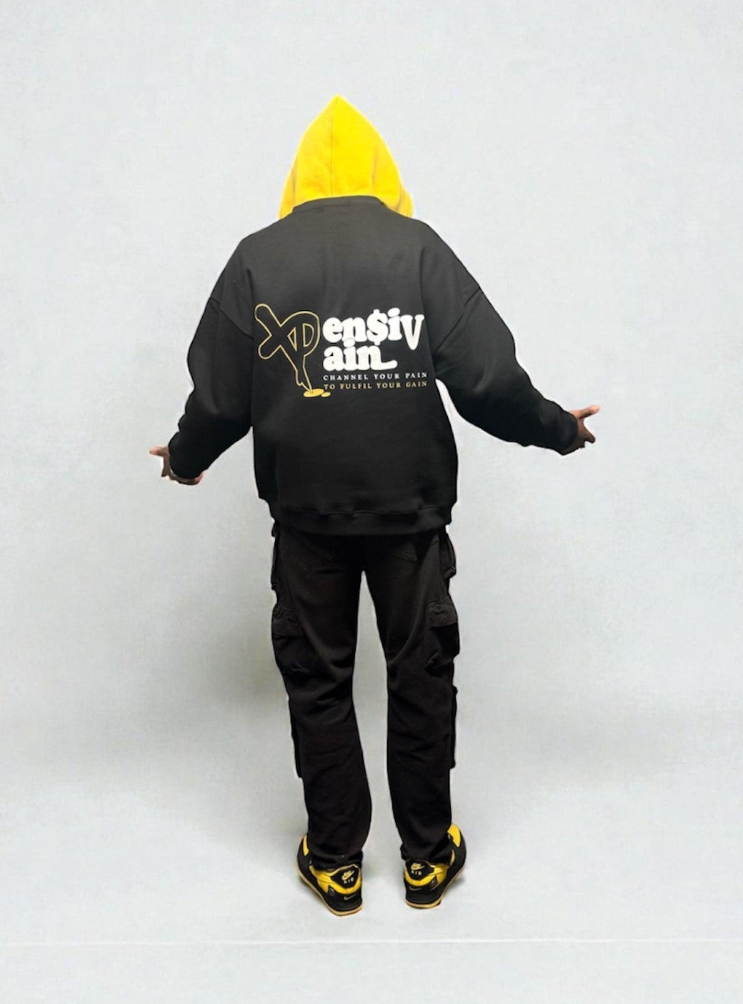 Back view of black XPensiv Pain sweatshirt with white and yellow graphic worn by male model.
