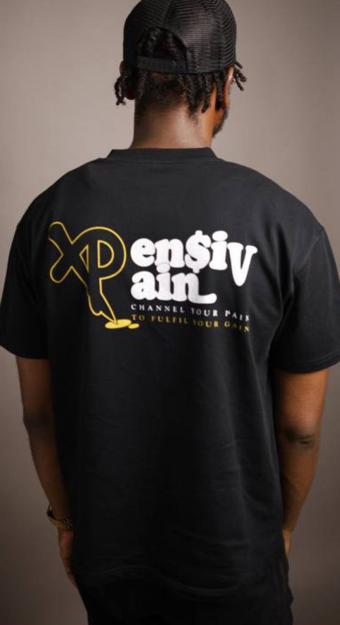 Back view of man wearing black XP London ‘XPensiv Pain’ t-shirt with yellow and white logo and slogan ‘Channel your pain to fulfil your gain,’ studio streetwear photo.