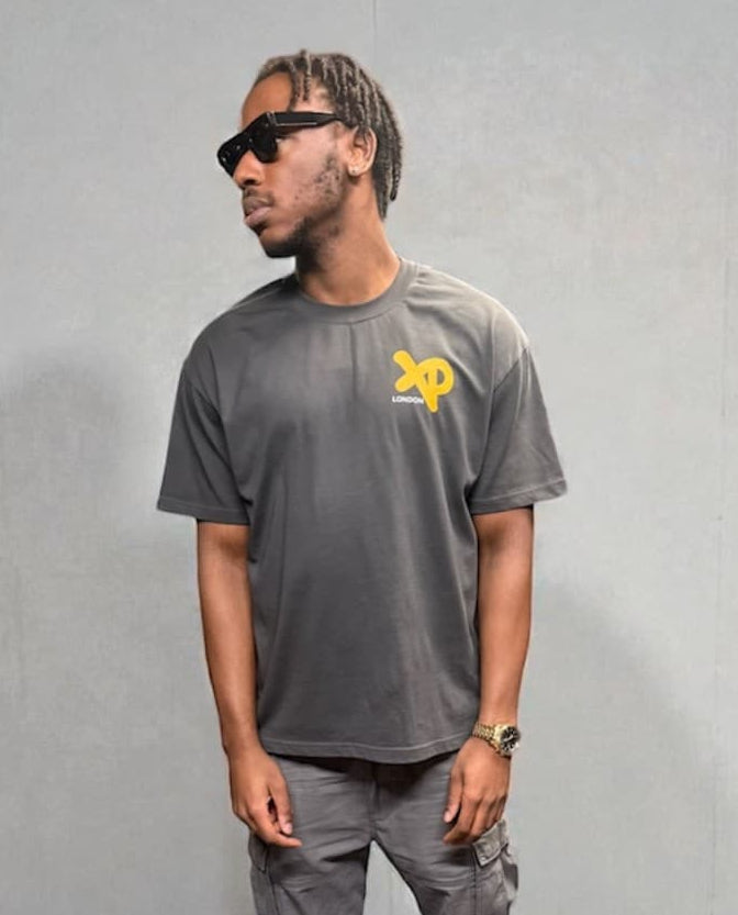 Model wearing grey XP London T-shirt with yellow chest logo, styled with cargo trousers