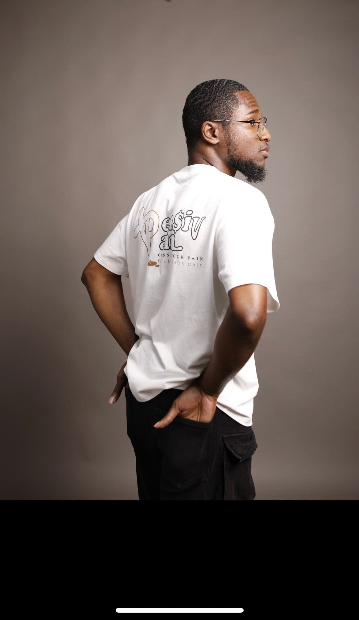 Back view of model wearing a white XP London ‘XPensiv Pain’ t-shirt with slogan ‘Channel your pain to fulfil your gain,’ minimalist studio streetwear photo.