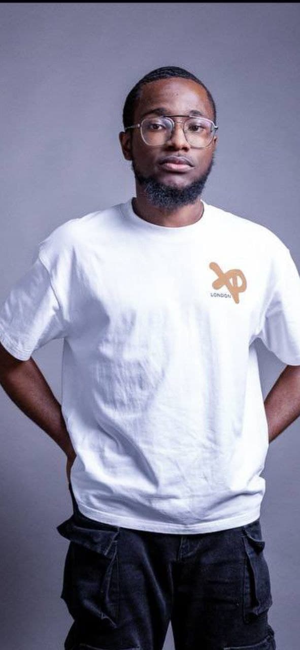 Model wearing a white XP London t-shirt with brown logo, styled with black cargo trousers, minimalist studio streetwear photoshoot.