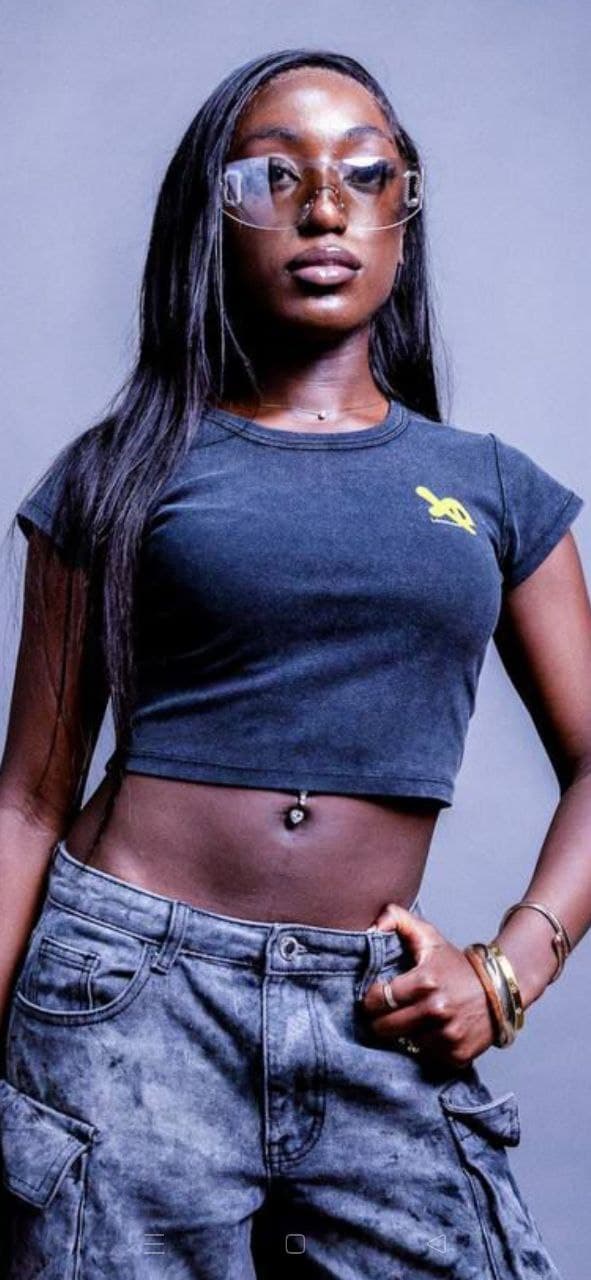 Woman wearing a charcoal-black XP London cropped t-shirt with yellow logo and cargo jeans, minimalist studio streetwear fashion portrait.