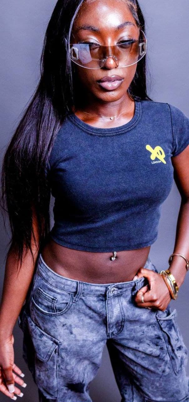 Woman wearing a charcoal-black XP London cropped t-shirt with yellow logo and grey cargo jeans in a studio photoshoot, showcasing urban streetwear style.