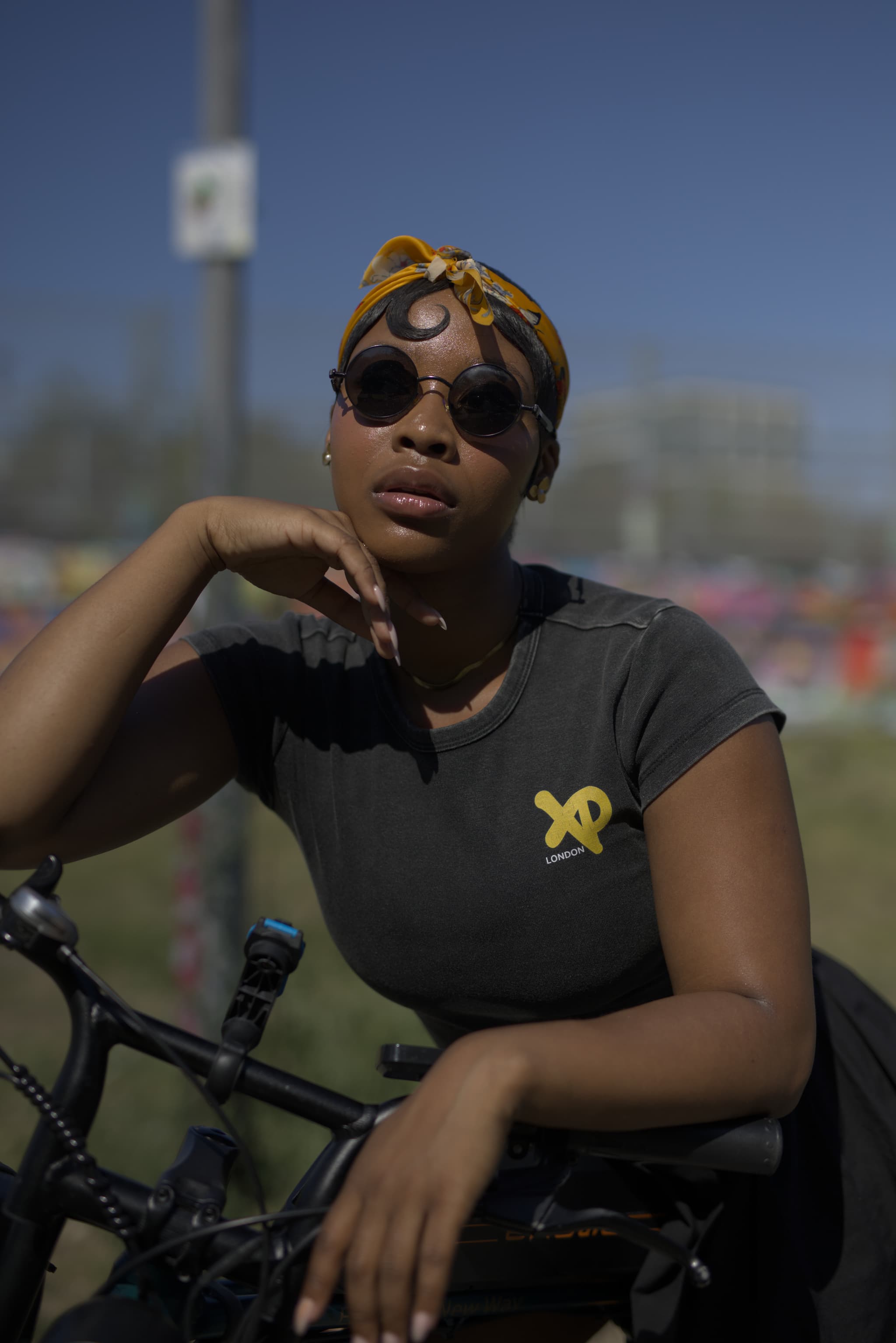 Close-up portrait of woman in XP London crop top leaning on bike with orange headband and sunglasses